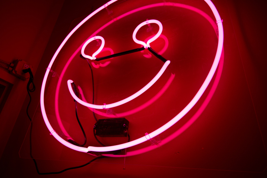 A photo of a pink neon light in the shape of a smiley face.